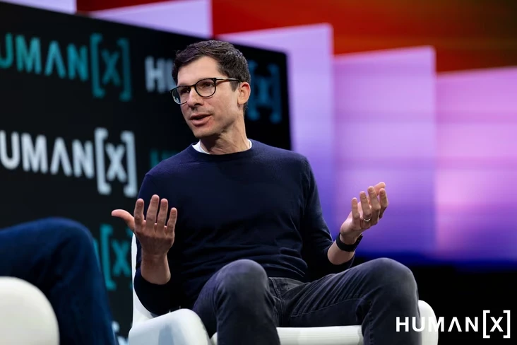 Sierra co-founder Clay Bavor speaking on stage with both hands open, in front of a HumanX backdrop